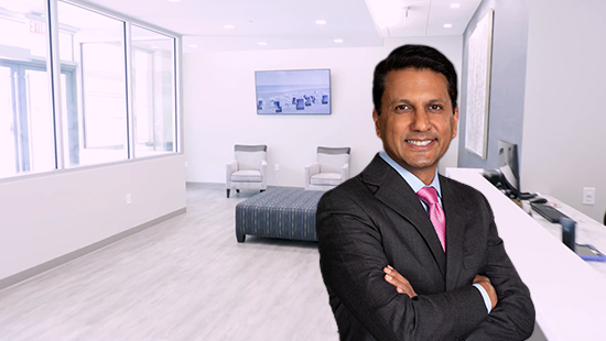 Dr. Sonny Goel standing in a Goel Vision office, wearing a suit and smiling, with a modern office interior in the background.