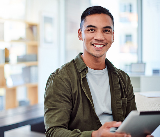 Smiling man using a tablet, representing the benefits of LASIK financing, including long-term savings and improved vision.