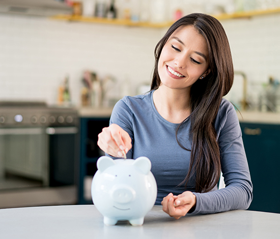 Smiling woman placing money into a piggy bank, symbolizing financing options for LASIK to make vision correction more affordable.