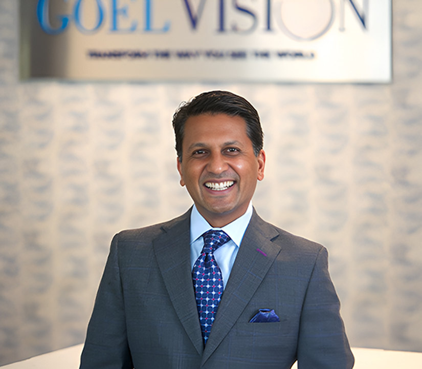 Dr. Sonny Goel, leading LASIK surgeon at Goel Vision, standing in front of the Goel Vision logo, smiling in a professional setting.